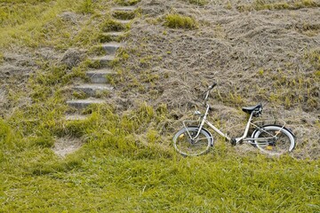 Abandoned bike on empty natural grass covered ground near stairs.  Conceptual life, environment and future theme.