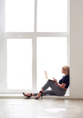 Young beautiful successful business woman is sitting in a big light trendy window and looking in her laptop. busy, attended,  successful. Business, home, finance. Copy space . Internet shopping