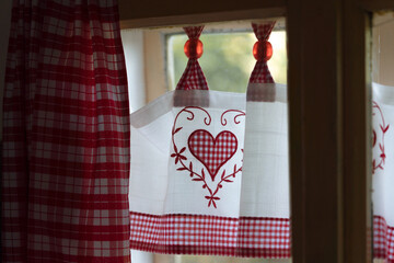 Interior of a room in an old house, looking out through a window with red and white lace curtains with heart,  weathered vintage window in an old cottage, Slovakia, Europe