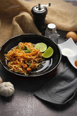 Pad Thai or Fried noodle Thai style, Thai style served with lime and seasonings. In a black palette, the visual style is dark tones.