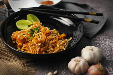 Pad Thai or Fried noodle Thai style, Thai style served with lime and seasonings. In a black palette, the visual style is dark tones.