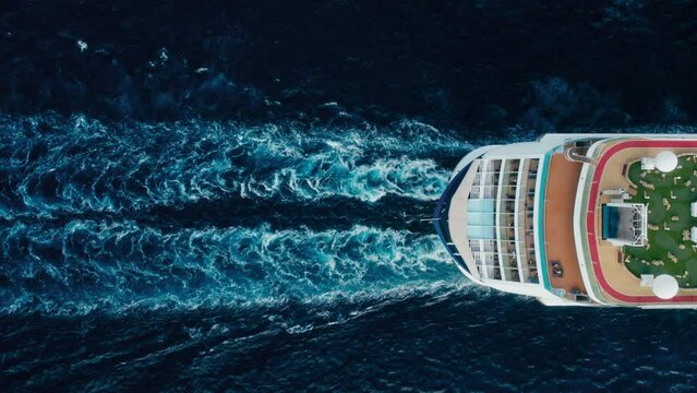 Top view on stern of a huge commercial passenger cruiser ship leaves traces on blue sea. 