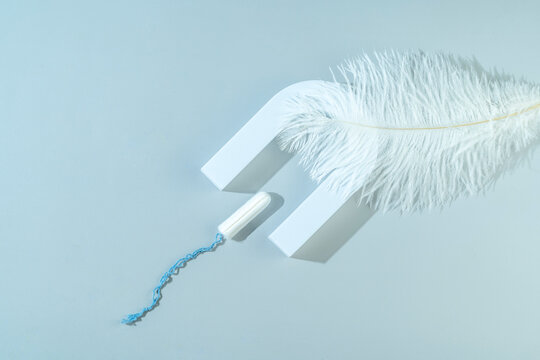 A woman personal hygiene cotton tampon lying on a light pink feather as a concept of freshness