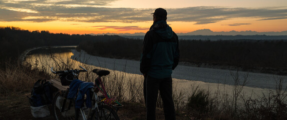 Man with mountain bike at sunset. Concept of adventure, freedom and outdoor recreation. Ticino Park and river Ticino near Castelnovate with Monte Rosa and the Alps in the background, Italy