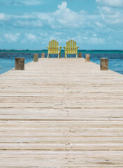 Two yellow chairs at the end of a wooden dock looking out over the Caribbean Sea on a sunny day.