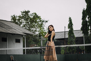 Beautiful female model, wearing a black tanktop, posing and stylish in the middle of a tennis court in the afternoon.