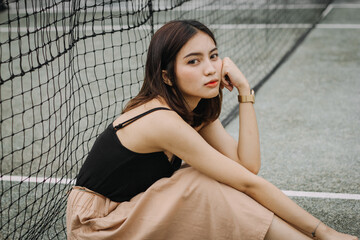 Beautiful female model, wearing a black tanktop, posing and stylish in the middle of a tennis court in the afternoon.