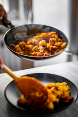 woman puts food from a frying pan into a plate