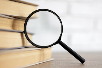 Fototapeta premium education and research concept - stack of books and magnifying glass on the table in library