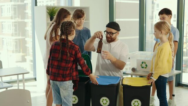 Garbage recycling children. Male teacher shows to the pupils how and where sort rubbish correctly on the garbage sorting class. People and ecological lesson.