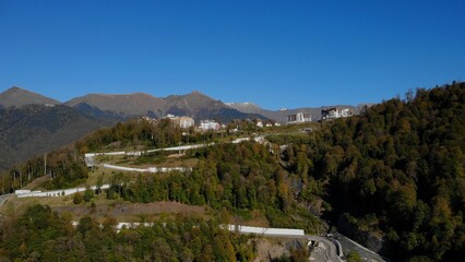 Cars drive on the mountain road leading to rosa khutor village. caucasian mountain peaks against clear sky. forest trees in bright autumn colors.