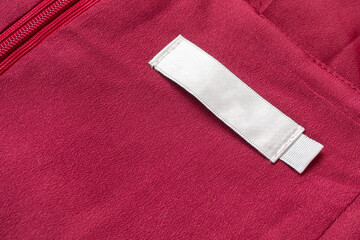Blank white laundry care clothes label on red fabric texture background