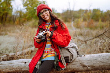 Beautiful woman taking pictures  in the autumn forest. Smiling woman enjoying autumn weather. Rest, relaxation, lifestyle concept.