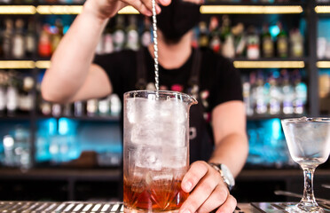 The bartender uses a bar spoon to stir the ice in a glass to cool it faster.