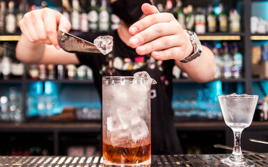The bartender uses a spatula to fill the glasses with ice to cool them down before serving the cocktail.