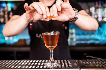 Bartender decorates cocktail with lemon or orange peel.