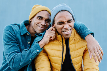 African American twin brothers playing with each other with love an affection, wearing funny blue and yellow trendy clothes