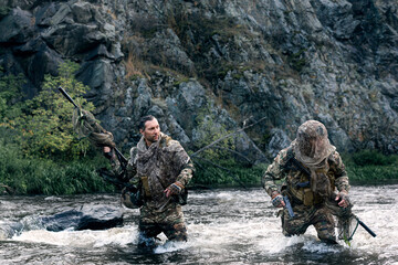 Modern warfare concept - two mercenary soldiers crossing the river after the completion of the...