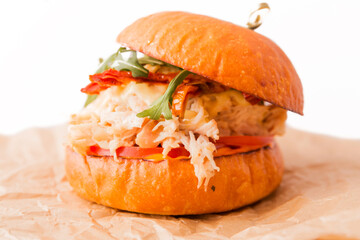 Burger with chicken fillet, pineapple, arugula, tomatoes, bacon and sauce on a wooden plate on a white background