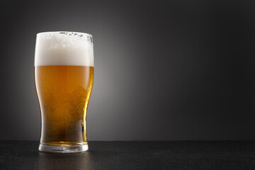 Draught beer in glass on a granite stone with copy space. Full glass of fresh golden and cold beer on dark gray background. Selective focus