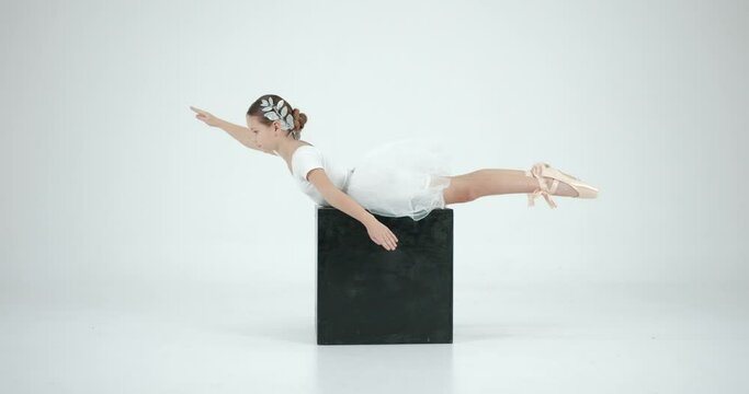 Little ballerinaposing on a black cube in studio