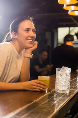 A beautiful girl is relaxing in a bar with a glass of cocktail in her hand. The girl looks at the bartender and smiles