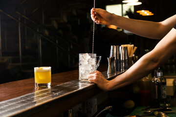The bartender uses a bar spoon to stir the ice in a glass to cool it faster.