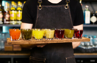 In bartender hands there is a colourful set of alcoholic cocktails in shot glasses shooters for an alcoholic party.