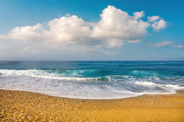 Fototapeta na wymiar Beautiful summer seascape with a turquoise sea, calm rolling wave with white foam, blue skies with clouds and strip of golden sandy beach.