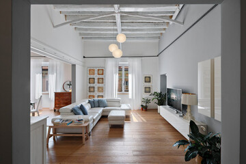 interior view of a modern living room, the sofa is in front of a tv cabinet, the floor and ceiling are made of wood, in the background the window