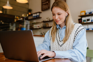 Blonde white woman listening music while working with laptop at cafe