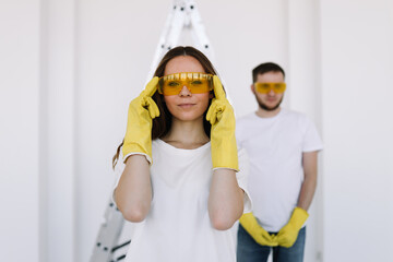 Portrait of a married man and woman in yellow safety glasses and gloves who have moved into a new house and are doing repairs on a isolated background. Couple renovates the interior using paint roller