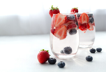 Mineral infused water or mocktail in a glass with strawberry and blueberry on white background with copy space