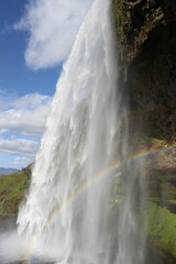 Fototapeta premium Vertical shot of a wonderful view of a rainbow against a waterfall during daytime in Iceland