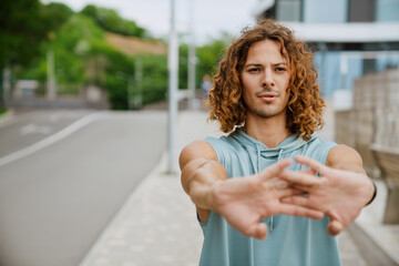 Young athletic long-haired handsome serious man stretching his arms