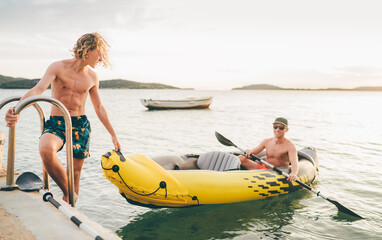Father with teenager son on the bright yellow inflatable kayak returning back from evening ride by the Adriatic sea harbor in Croatia near from Sibenik city. Vacation and family values vertical image.