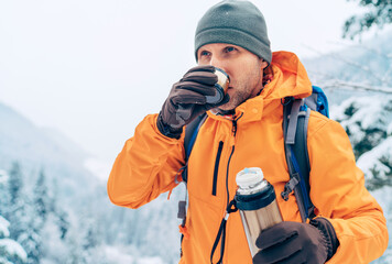 Man drinking a hot drink from thermos flask dressed bright orange softshell jacket while he...