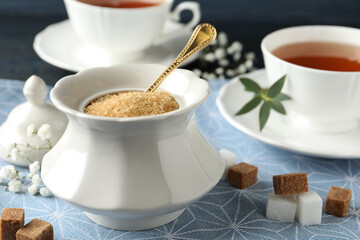 Ceramic bowl with brown sugar and cups of tea on table