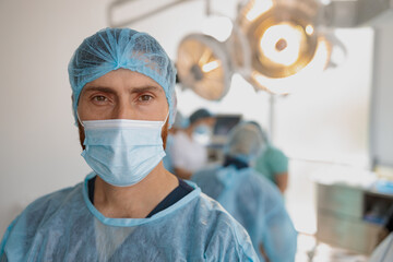Fototapeta na wymiar Close up of doctor in mask standing in operating room before surgery on background of colleagues