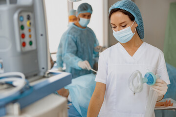 Nurse holding breathing mask for anesthesia standing in operation room with colleagues on background