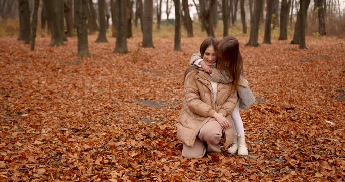 Mom hugging with daughter in autumn park