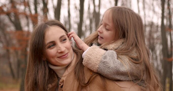 Beatiful mom holding daughter piggyback in forest