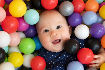 Fototapeta na wymiar Portrait of a Caucasian baby happy face. Healthy baby in the ball pit playing with colorful plastic balls.