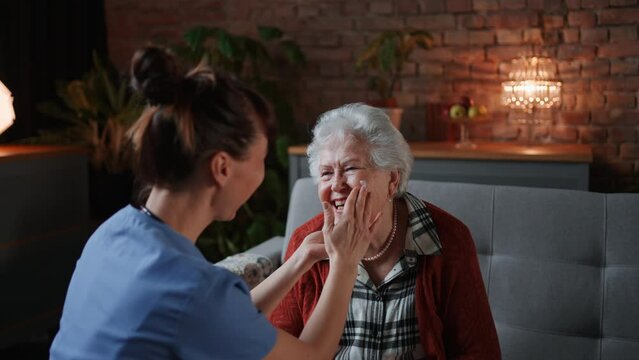 Female healthcare worker or caregiver visiting senior woman indoors at home, doing body care to patient.