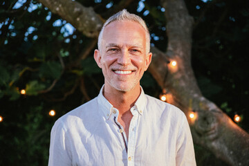 Close up ortrait of happy mature man with gray hair looking and smiling at camera outdoor at sunset in a backyard. Lifestyle concept. High quality photo