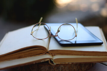 Stack of open books, e-reader and reading glasses in the garden. Selective focus.