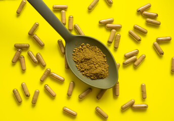 kratom pills composition on yellow background with kratom filled spoon, top view, flat lay