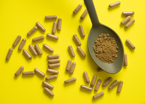 kratom pills composition on yellow background with kratom filled spoon, top view, flat lay
