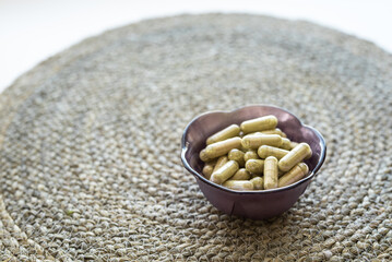 handful of green kratom pills capsules inside of small purple  pot on wicker surface