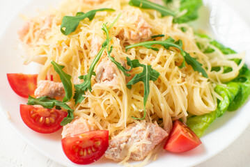 Spaghetti with salmon, cheese on a lettuce salad sprinkled with arugula and cherry tomatoes close-up.